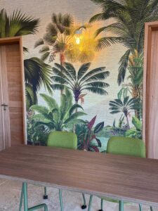 Salle de séminaire 'Salle Amazonie' à l'Habitation Saint Charles, avec une table en bois, des chaises vertes et un papier peint tropical.